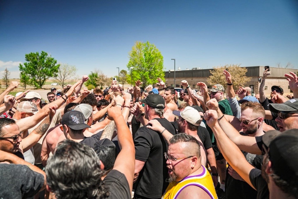Men outdoors under clear sky lifting hands and fists in unified prayer at Launching Pad