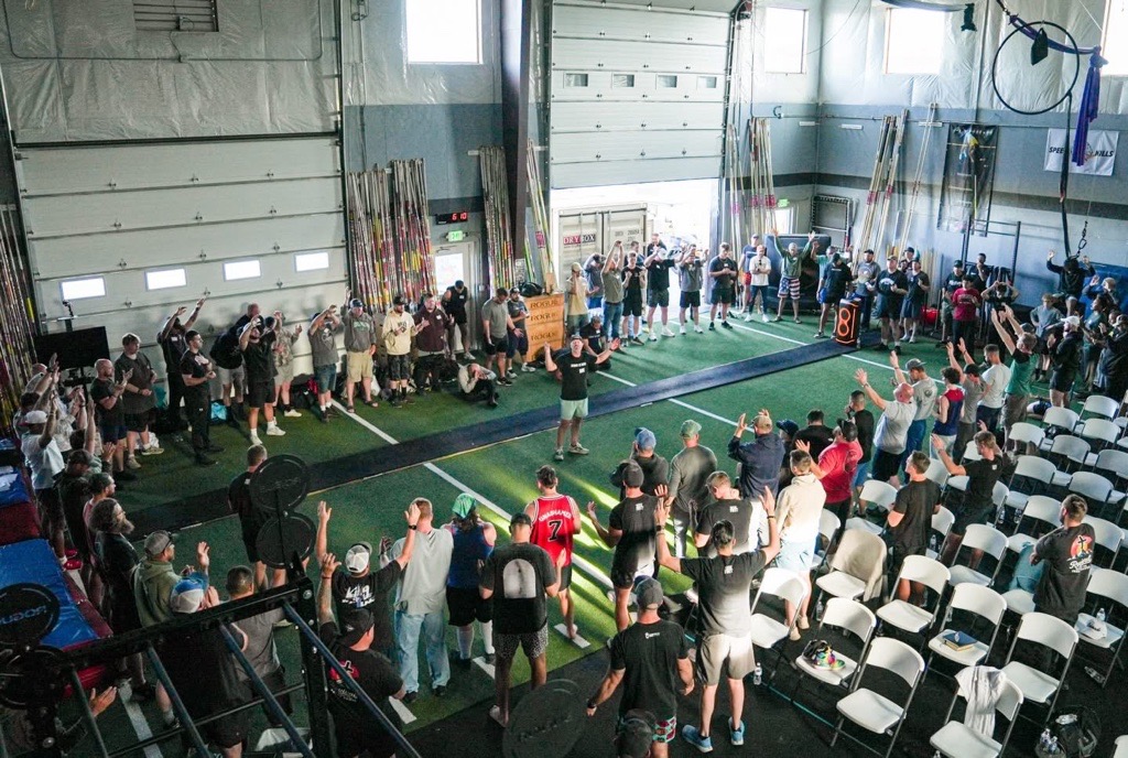 Large group of men standing in prayer with hands raised inside the CrossFit ELM gym at Colorado Launching Pad